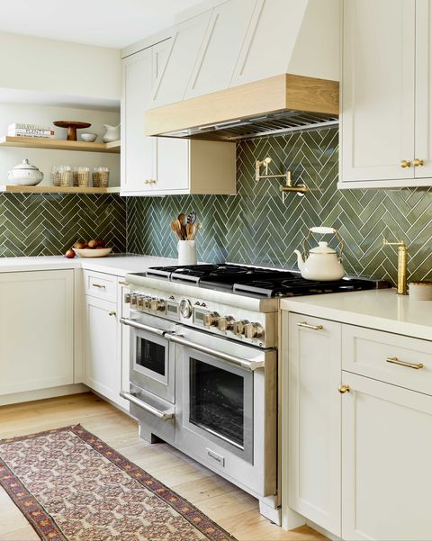 kitchen, cream cabinets with cream marble countertop, green tile backsplash, floor runner, stainless steel oven, gold hardware