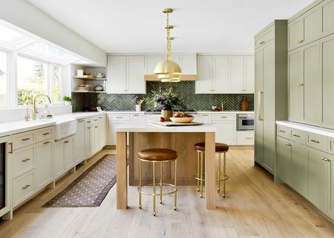 sunny kitchen with cream cabinets, green olive cabinets for storage, wooden kitchen island, brown leather stools, gold hardware