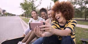 Playful teenage girl friends with skateboards taking selfie with camera phone