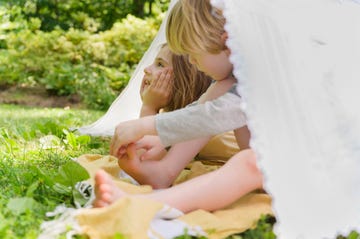 girl 6 7 and boy 4 5 relaxing in homemade tent in backyard