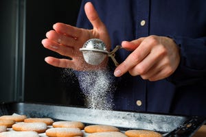 girl baker or woman pastry chef sprinkled with powdered sugar from a strainer cookies in the shape of a heart, on baking paper, on the background of a wooden kitchen table cooking concept, valentine's day, christmas, mother's day and thanksgiving