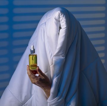 een vrouw verstopt onder een dekbed en heeft cbd olie in haar hand