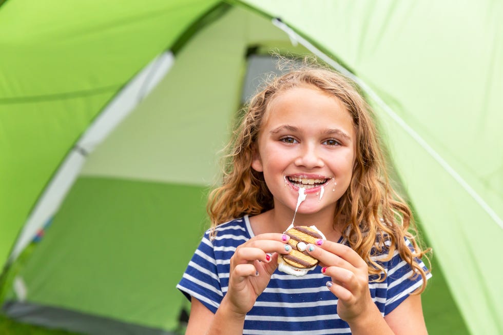girl eating messy s'more by green camping tent