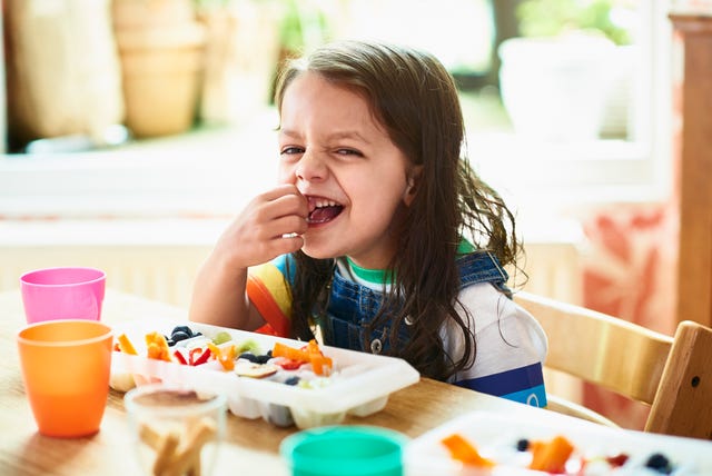 una niña sonríe mientras toma un snack saludable compuesto por crudités de verduras