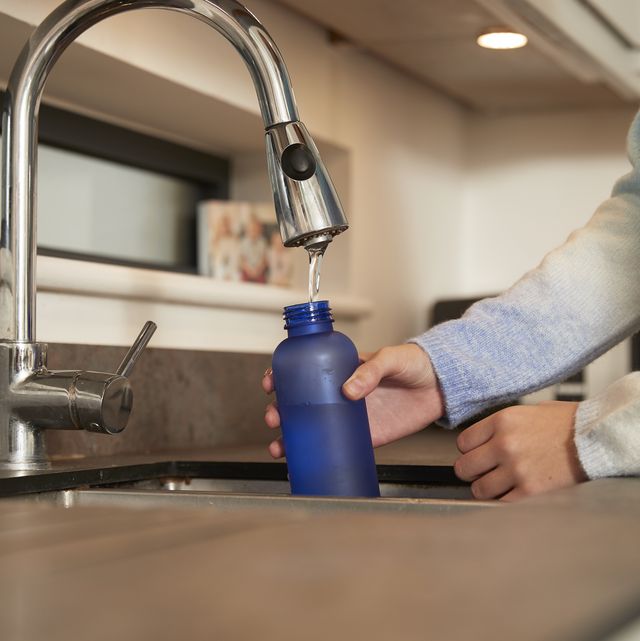 girl filling reusable bottle with water from faucet