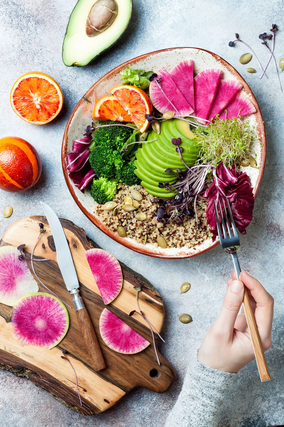 girl holding fork and eating vegan, detox buddha bowl with quinoa, micro greens, avocado, blood orange, broccoli, watermelon radish, alfalfa seed sprouts
