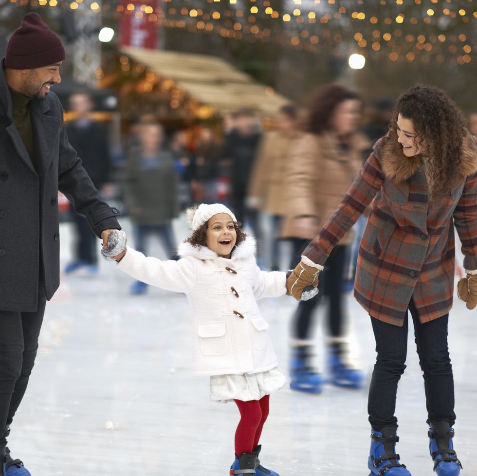 girl holding parents hands ice skating, smiling