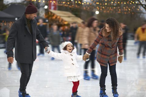 girl holding parents hands ice skating, smiling