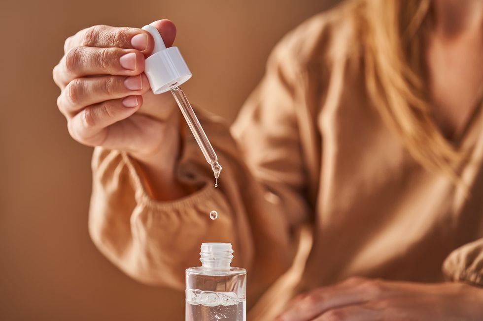 a girl in a beige dress holds a pipette with a drop of serum in her hands