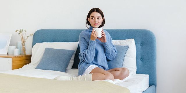 Girl in a blue sweater in interior Hygge style with a cup of hot tea in her hands sits on the bed