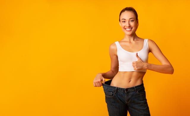 girl in oversize jeans gesturing thumbs up smiling, yellow background