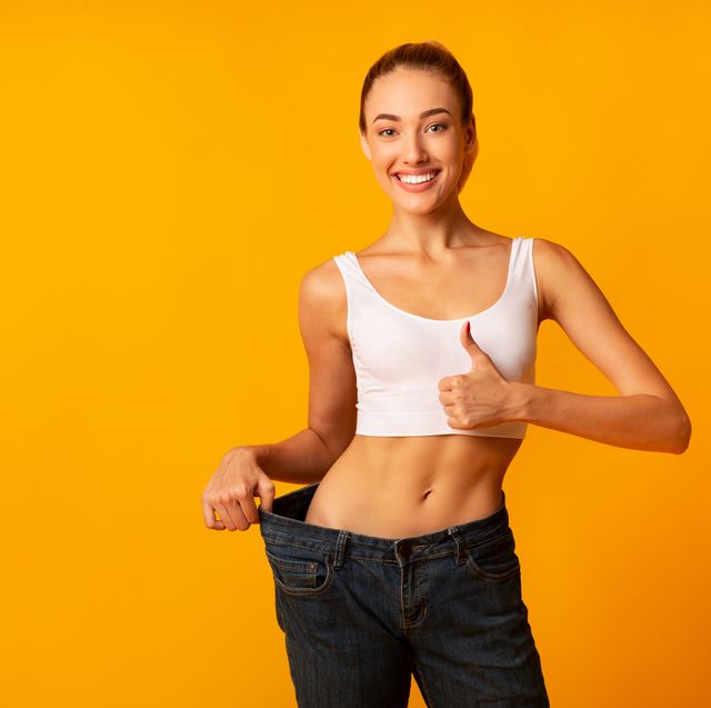 girl in oversize jeans gesturing thumbs up smiling, yellow background