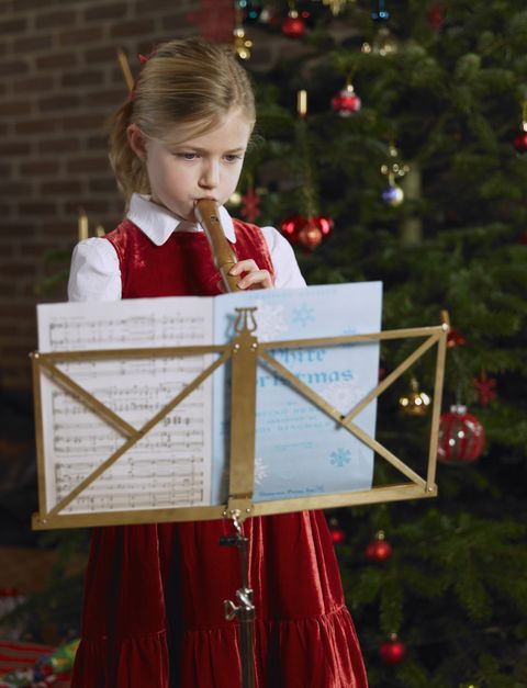 girl wearing a red dress playing recorder in front of christmas tree