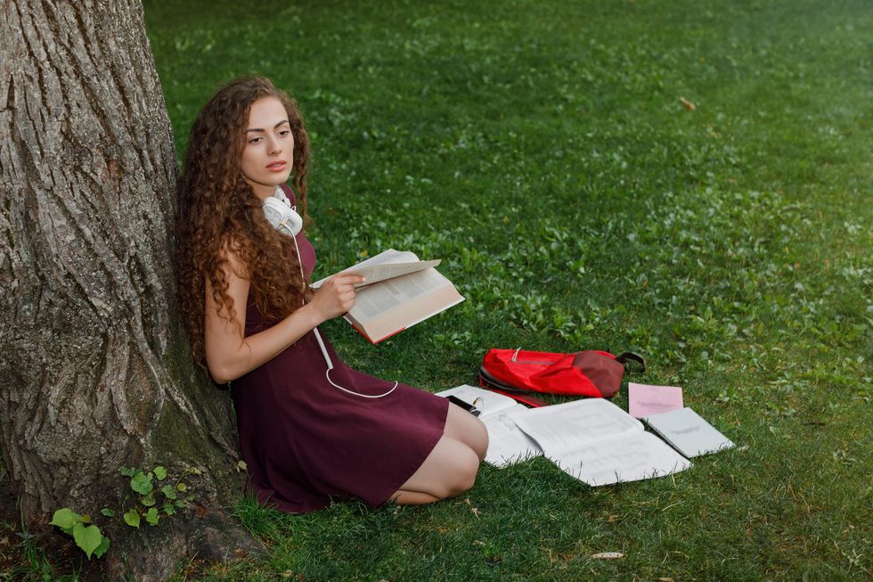 girl student holding book and sitting under tree
