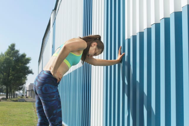 Girl training, resting against blue wall, city