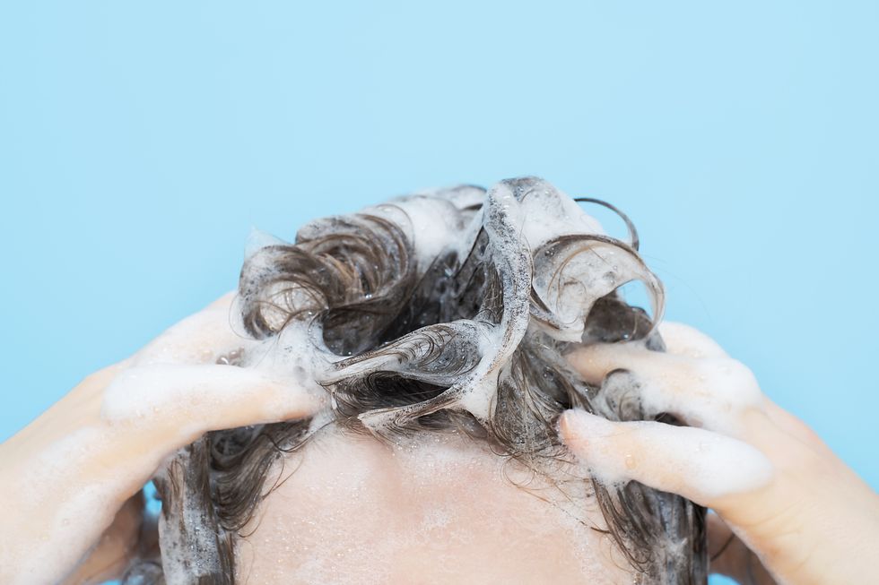 a girl washes her hair with shampoo on blue background, front view