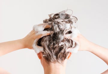 a girl washes her hair with shampoo on white background, back view