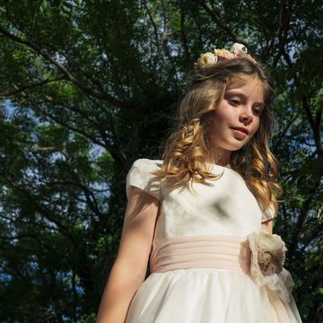 girl wearing communion dress standing under tree