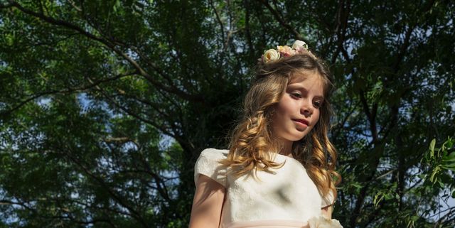 girl wearing communion dress standing under tree