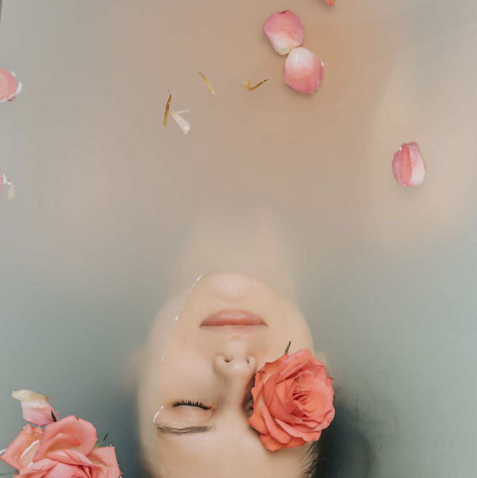 girl with eyes closed taking bath with roses in bathtub