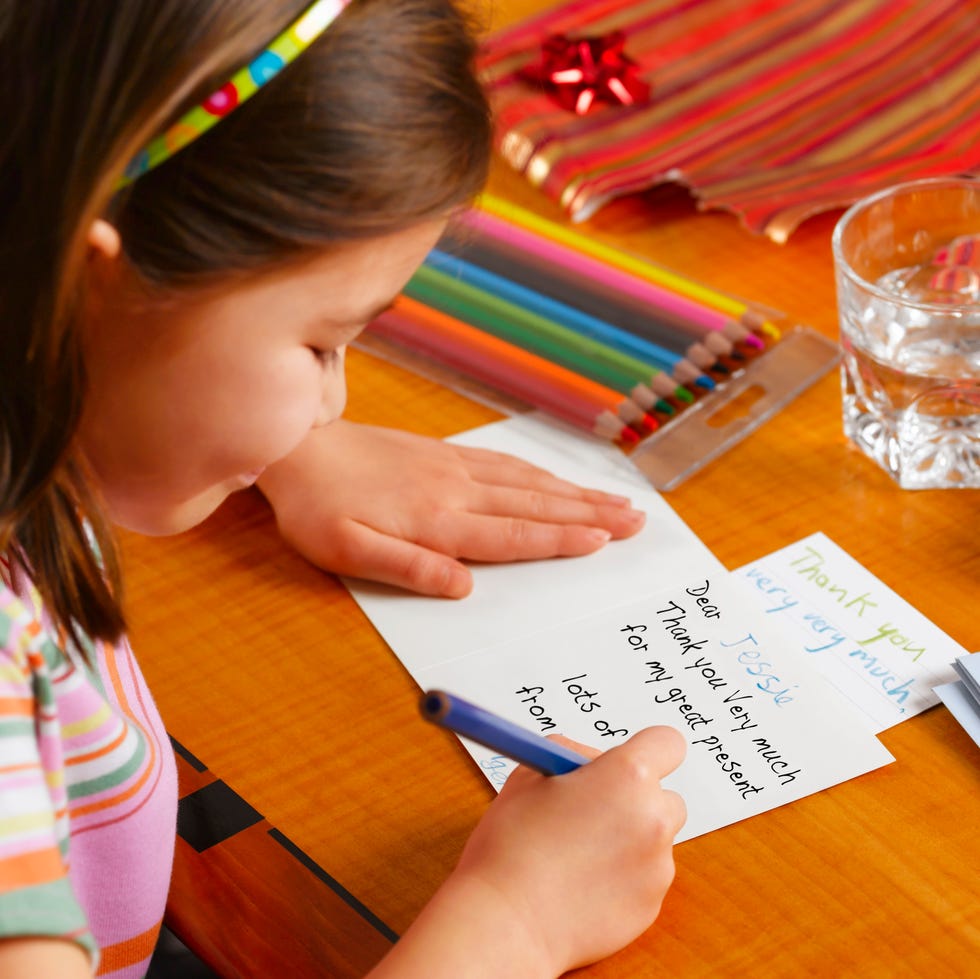 a white girl writing a thank you card with colored markers nearby