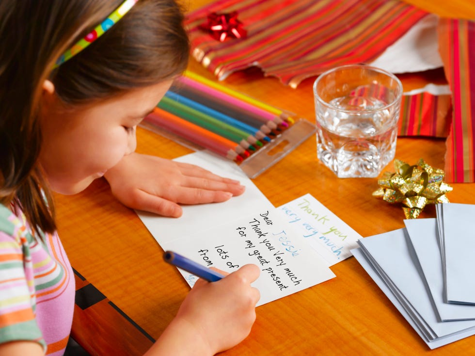 a little girl smiling while she writes a thank you card