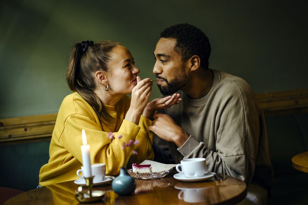 girlfriend feeding bite of dessert to her boyfriend at cafe