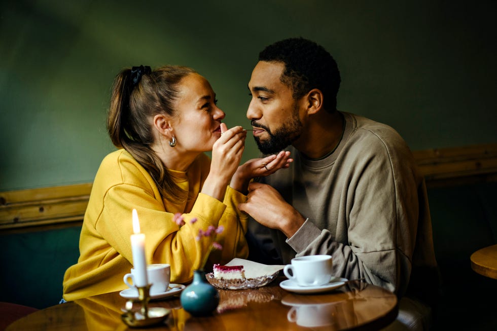 girlfriend feeding bite of dessert to her boyfriend at cafe