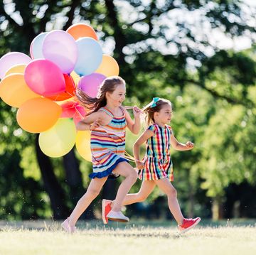 two laughing little girls running in the park with a bunch of colorful balloons sisters