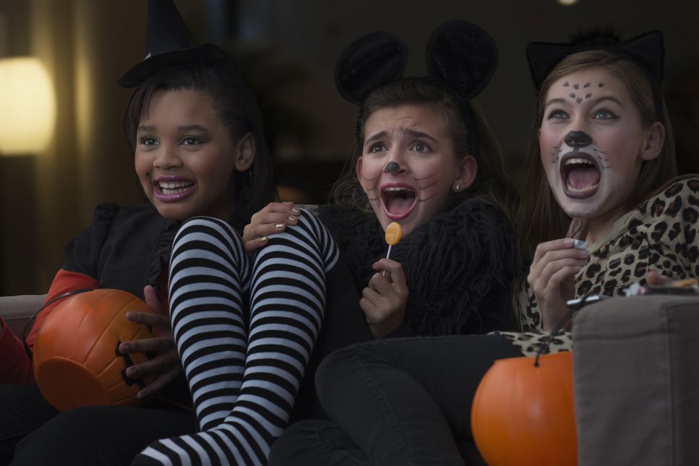 girls in costumes watching scary movie together on halloween