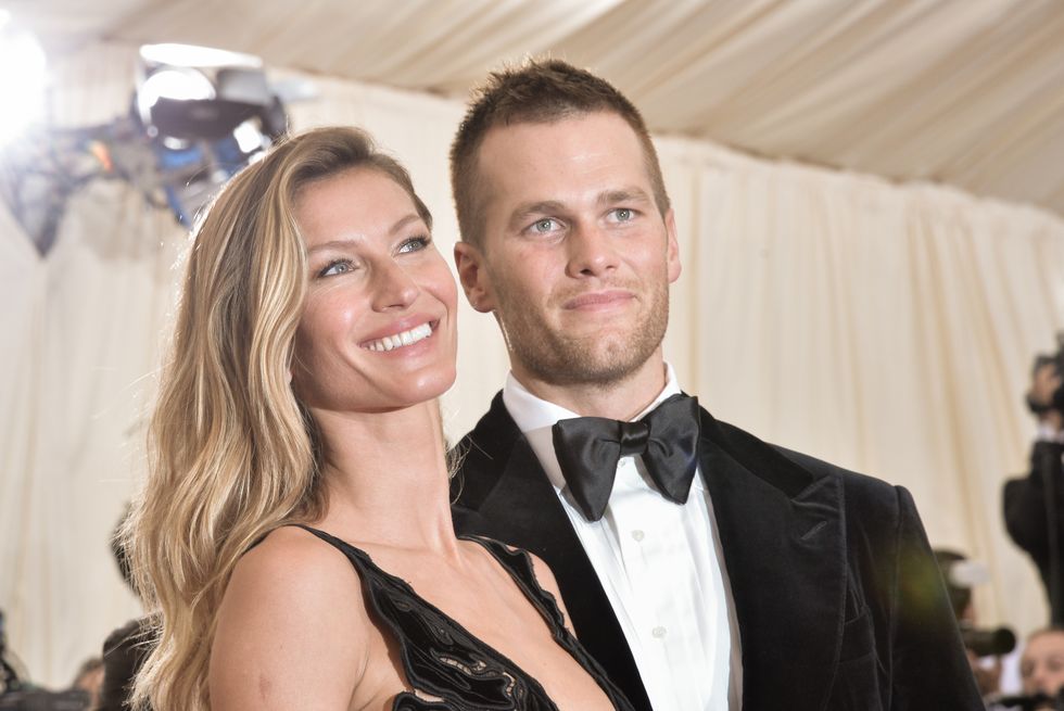 gisele bundchen and tom brady stand together for photos and look to the right, she wears a sleeveless deep cut dress, he wears a tuxedo