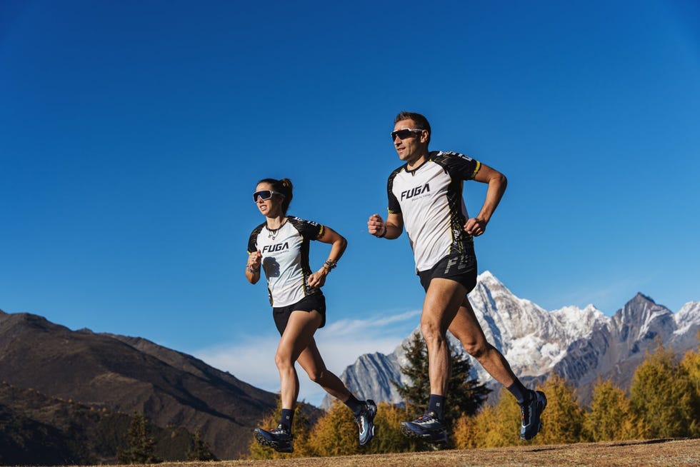 two runners in athletic gear running outdoors with mountain backdrop
