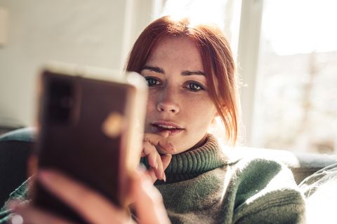 woman with red hair looking on screen of her mobile phone