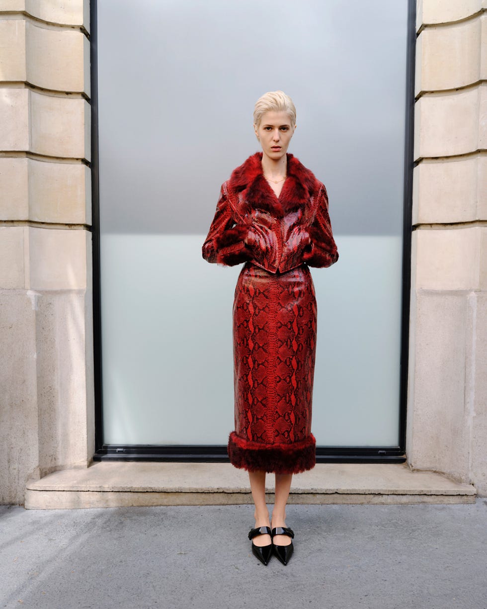 Fashion model in a bold red snakepatterned outfit with a fur collar and hem standing in front of a glass wall