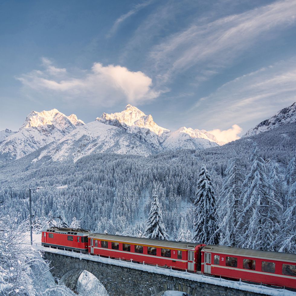 red bernina express train traveling on viaduct in the winter forest covered with snow, tarasp, graubunden canton, engadin, switzerland