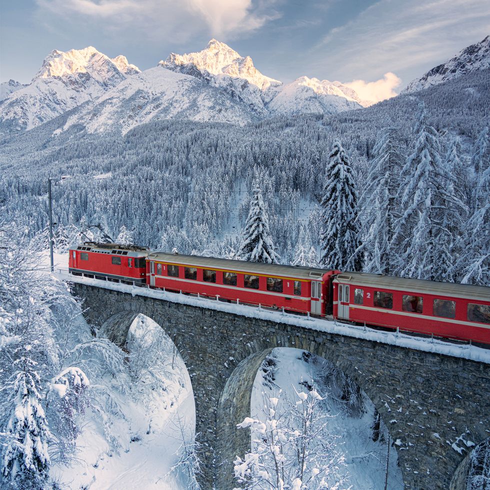 red bernina express train traveling on viaduct in the winter forest covered with snow, tarasp, graubunden canton, engadin, switzerland