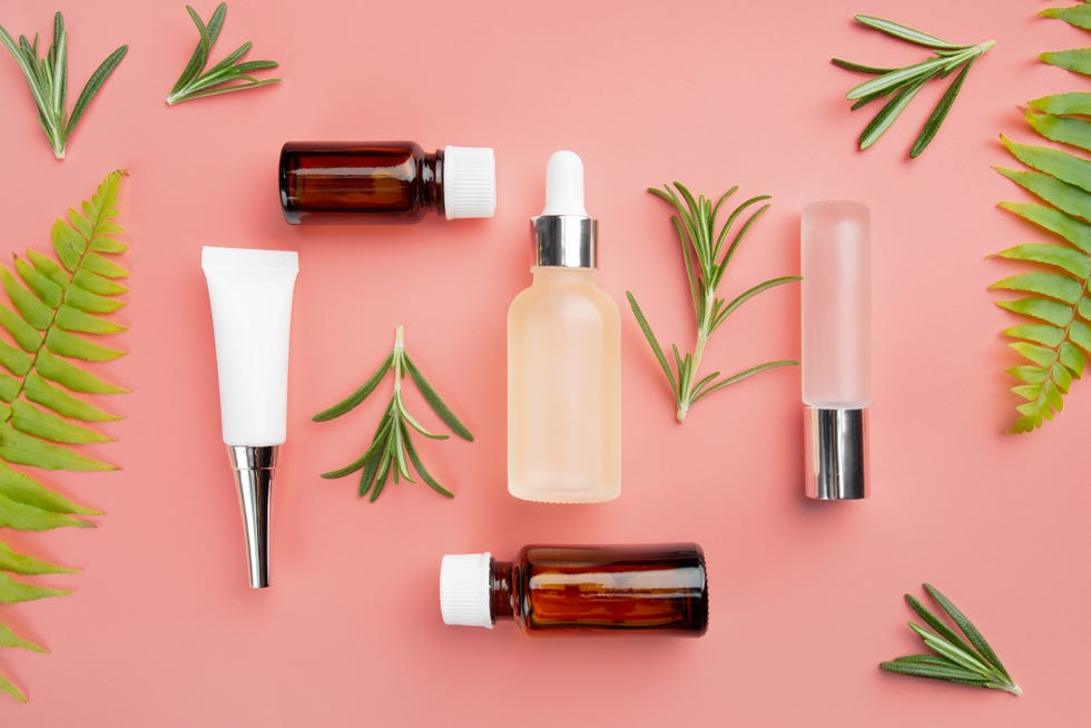 glass and plastic cosmetic bottles on pink background with rosemary leaves