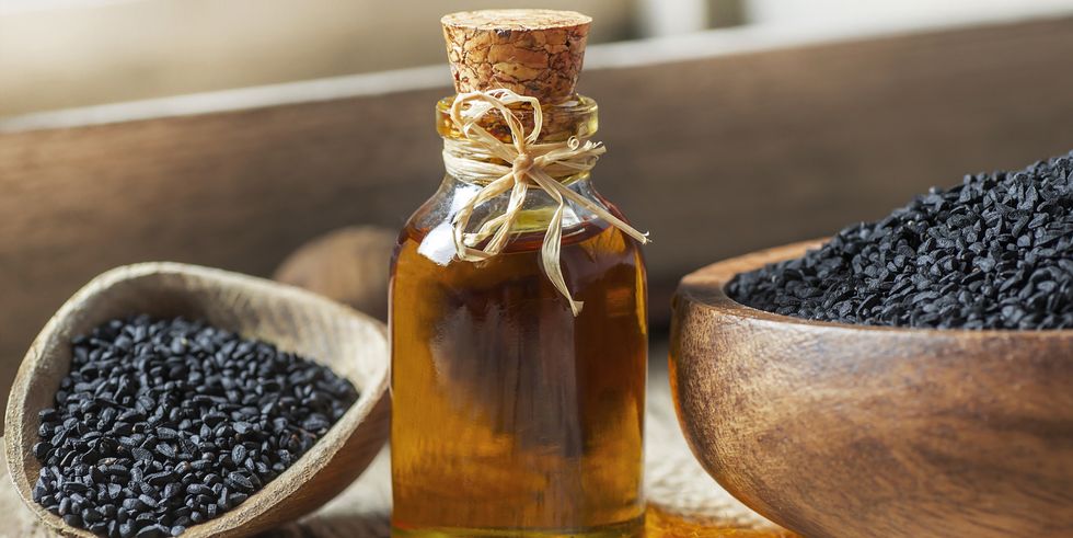 glass bottle of black cumin seeds essential oil , nigella sativa in spoon on wooden background