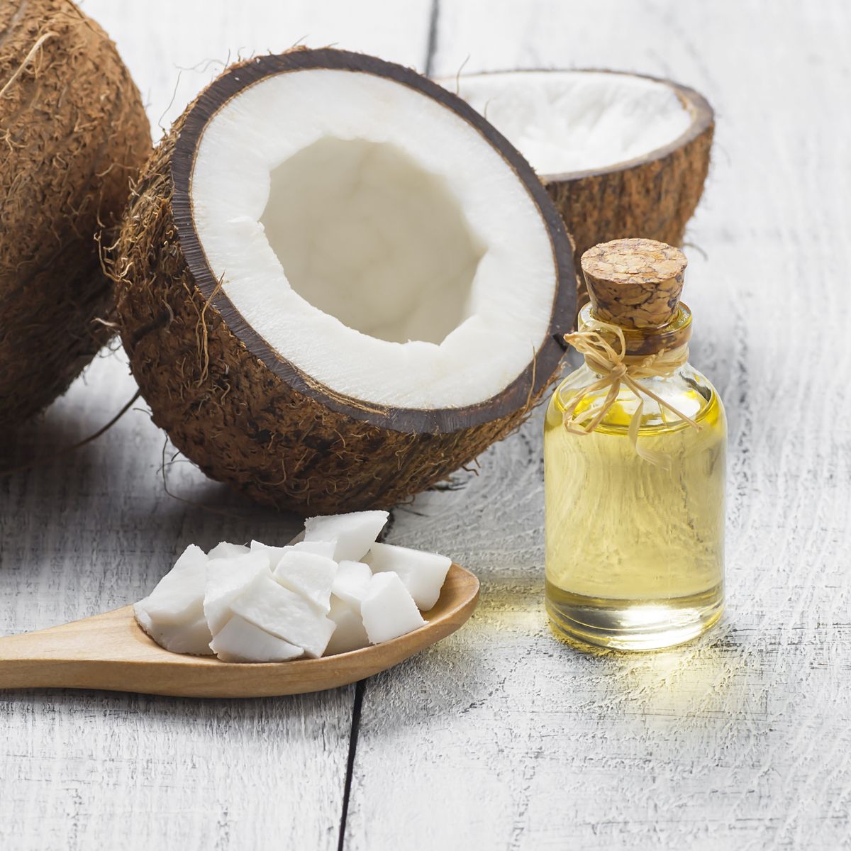 glass bottle of coconut oil with fresh coconut fruit on rustic background, alternative theraphy medicine concept, cocos nucifera