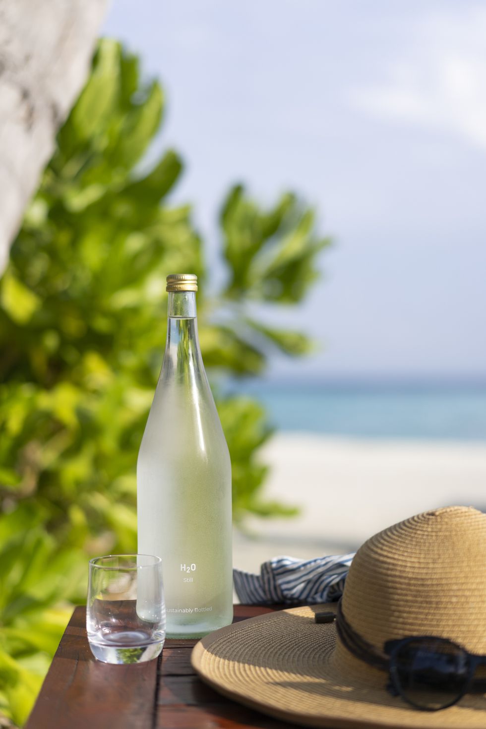 glass bottle of water, straw hat and sun glasses on the background of the beach in the maldives