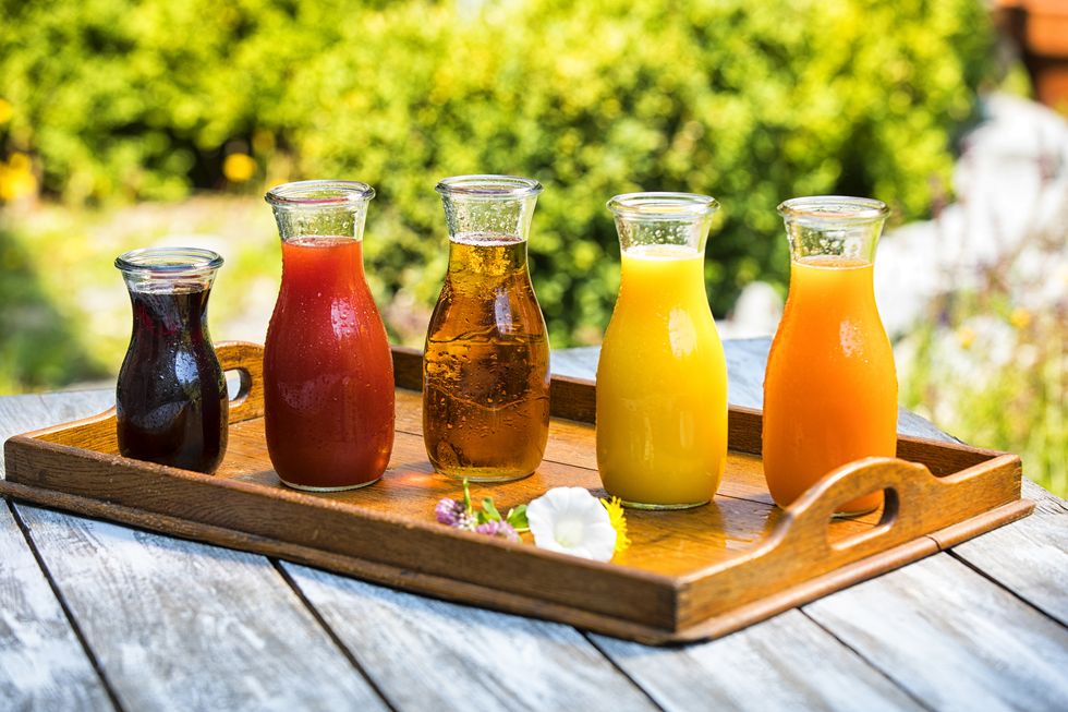 glass bottles of various fruit juices on wooden tray
