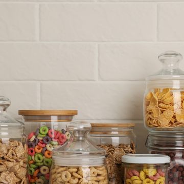 glass containers with different breakfast cereals on white countertop near brick wall