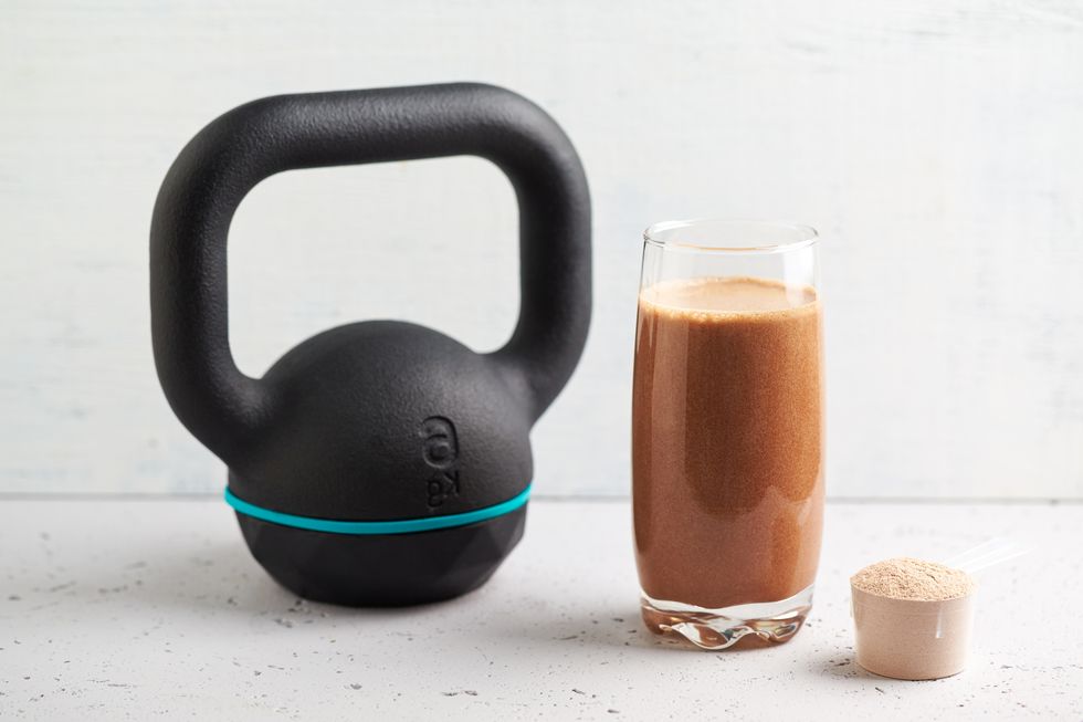 glass of chocolate protein shake with milk and banana, whey protein in scoop and black sporting kettlebell in background sport nutrition stone wooden background copy space