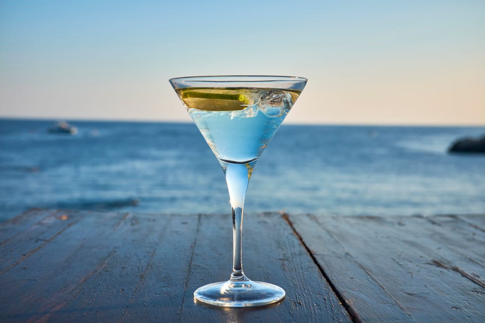 glass of ice cooled martini with lime slice in front of the sea