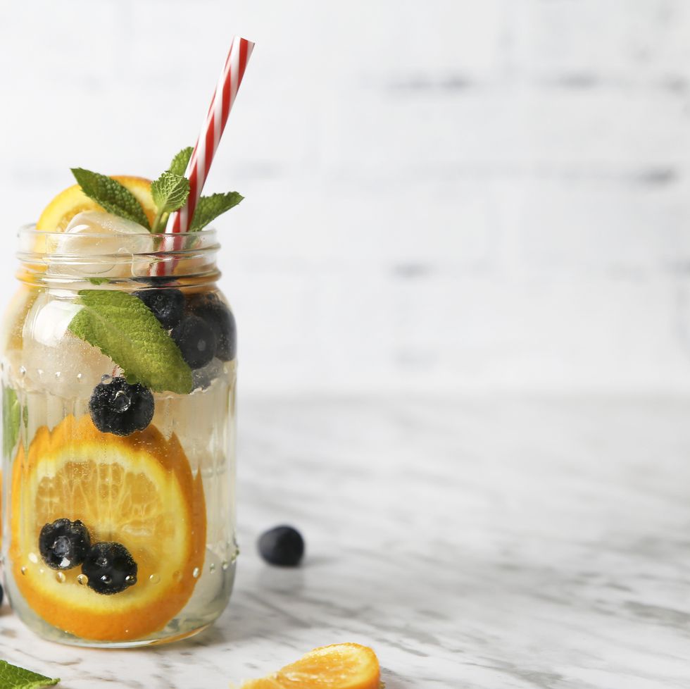 glass of infused water with orange, blueberries and mint on ice