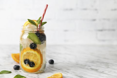 glass of infused water with orange, blueberries and mint on ice