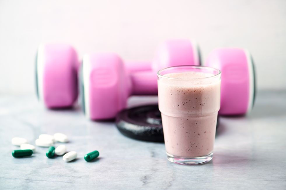 glass of protein shake with milk and raspberries bcaa amino acids, l   carnitine capsules and pink dumbbells in background sport nutrition stone  wooden background copy space