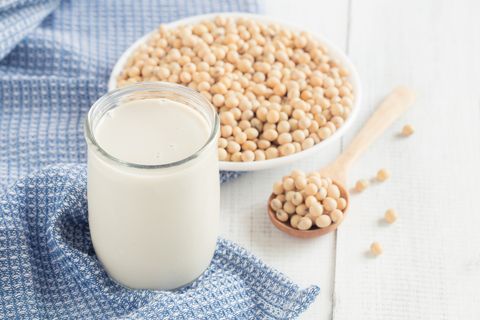 a glass of soy milk on a white wood floor with soybean as a background