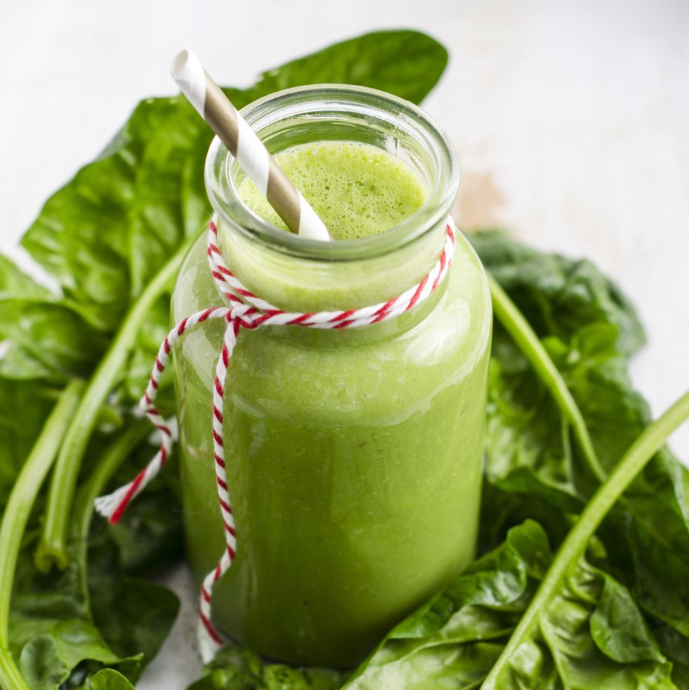 glass of spinach smoothie and spinach leaves on white wood