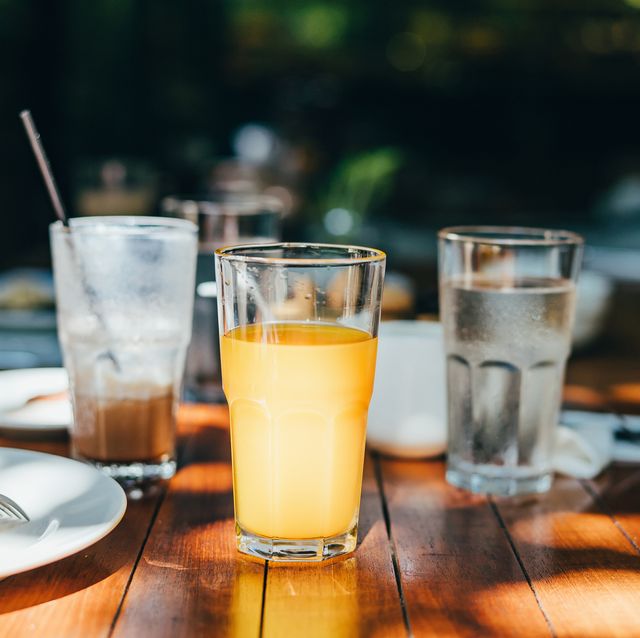 a glass of water, orange juice and coffee served on table in an outdoor restaurant against beautiful sunlight